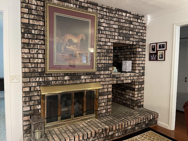 interior details with a textured ceiling, a fireplace, wood finished floors, baseboards, and ornamental molding