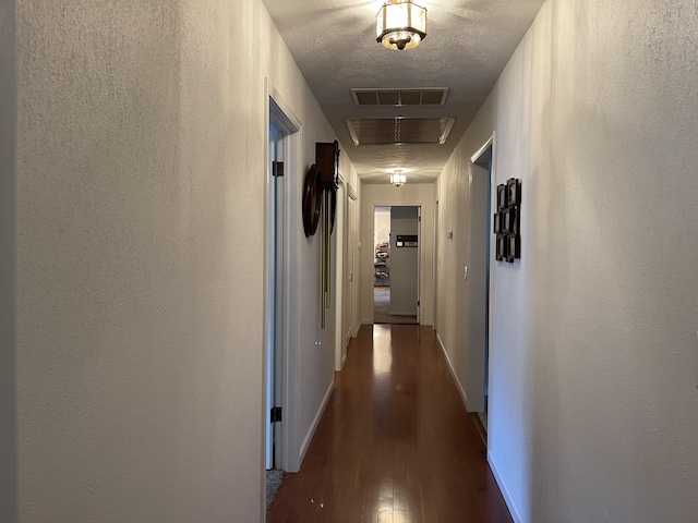 corridor with baseboards, visible vents, a textured wall, dark wood-style floors, and a textured ceiling