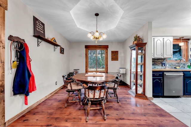 dining area with a notable chandelier, a tray ceiling, light hardwood / wood-style floors, and sink