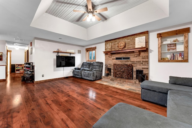 living room featuring ceiling fan, a brick fireplace, dark hardwood / wood-style flooring, and a tray ceiling