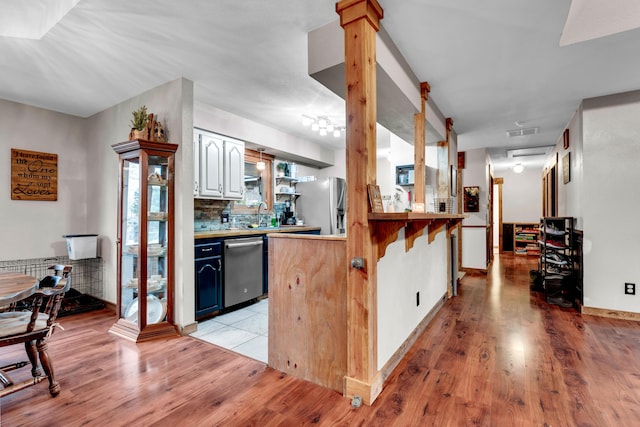 kitchen with appliances with stainless steel finishes, decorative columns, tasteful backsplash, kitchen peninsula, and light wood-type flooring