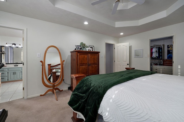 carpeted bedroom with sink, ceiling fan, ensuite bathroom, a spacious closet, and a raised ceiling