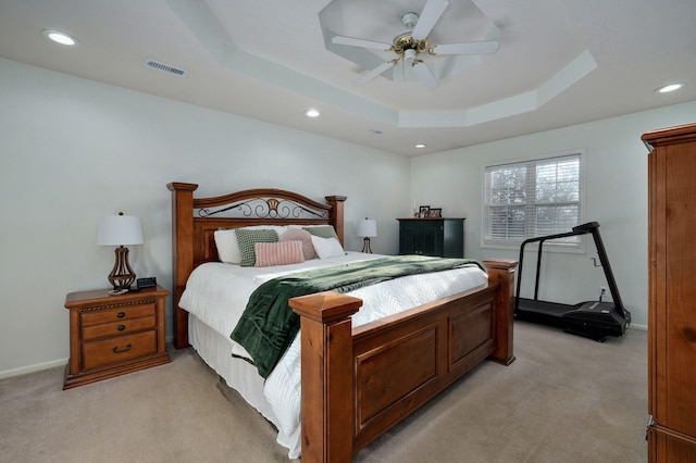 bedroom with a raised ceiling, light colored carpet, and ceiling fan