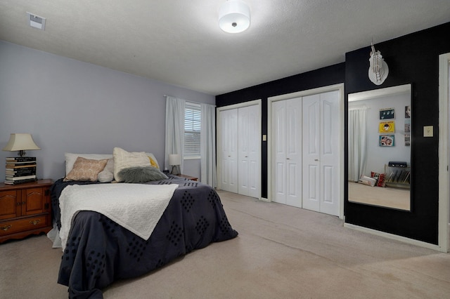 bedroom with two closets, light colored carpet, and a textured ceiling