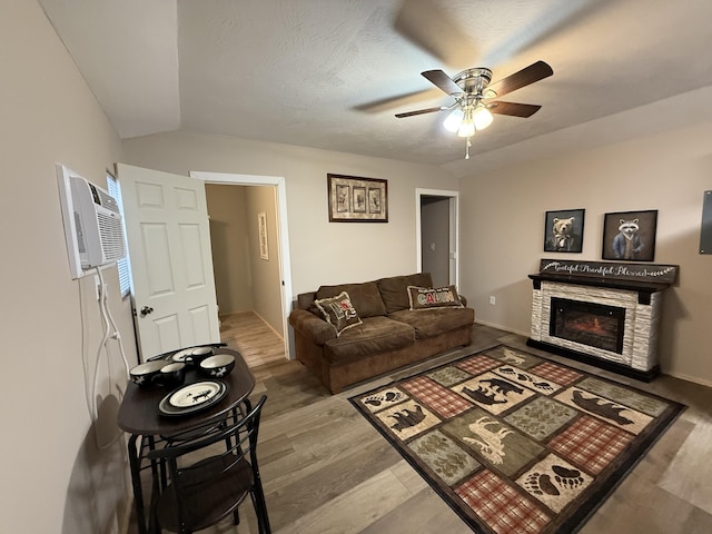 living room featuring lofted ceiling, a stone fireplace, a wall mounted air conditioner, ceiling fan, and hardwood / wood-style floors