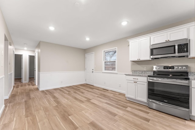 kitchen featuring white cabinetry, light wood-type flooring, light stone countertops, and appliances with stainless steel finishes