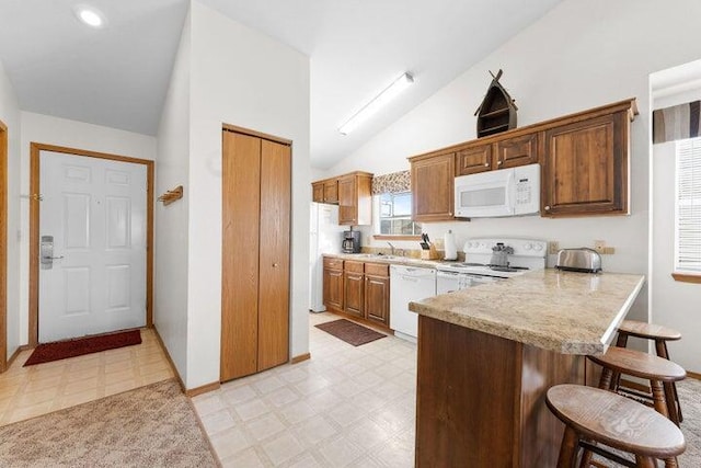 kitchen featuring lofted ceiling, sink, a kitchen breakfast bar, kitchen peninsula, and white appliances