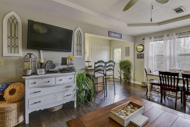 living room with ceiling fan, dark hardwood / wood-style floors, a textured ceiling, and a tray ceiling