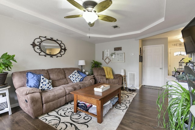 living room featuring dark wood-type flooring, ceiling fan, and a tray ceiling