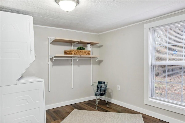 laundry area featuring dark wood-type flooring, stacked washer and dryer, and plenty of natural light