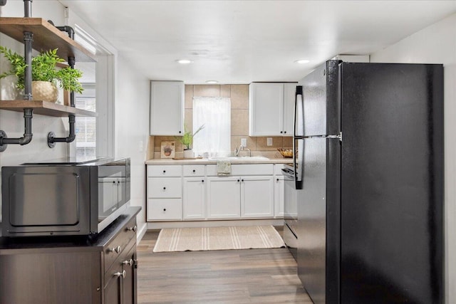 kitchen with tasteful backsplash, white cabinetry, black fridge, and dark wood-type flooring