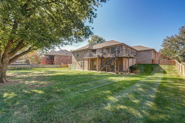 rear view of property with a trampoline, a wooden deck, and a yard