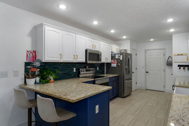 kitchen with a breakfast bar area, white cabinetry, stainless steel appliances, light stone countertops, and decorative backsplash