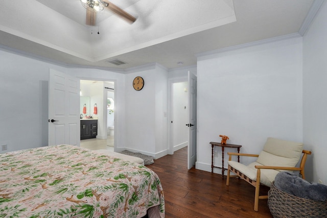 bedroom with connected bathroom, ornamental molding, a tray ceiling, dark hardwood / wood-style flooring, and ceiling fan