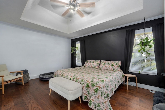 bedroom with dark hardwood / wood-style floors, a raised ceiling, and multiple windows