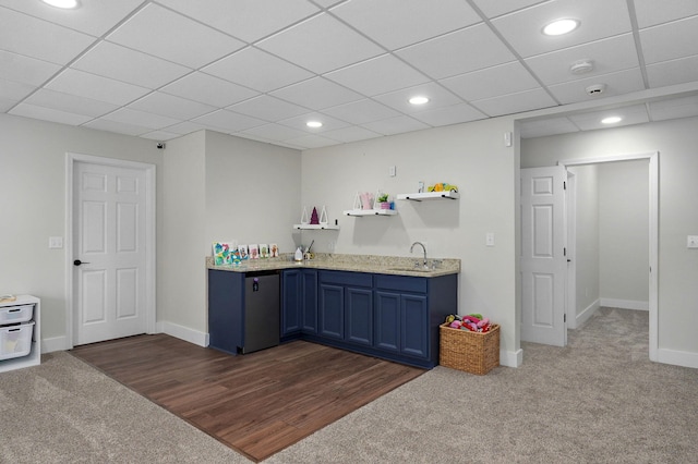 interior space with dark colored carpet, a paneled ceiling, blue cabinetry, and sink