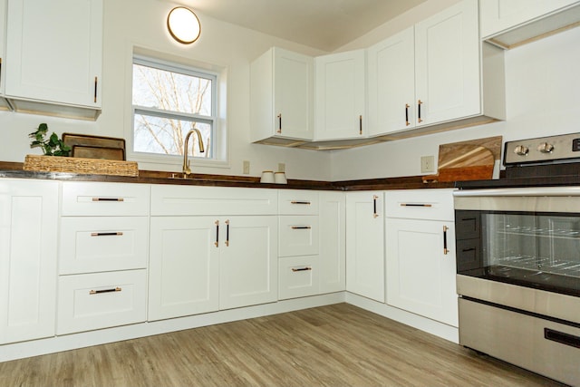 kitchen with stainless steel electric range oven, sink, white cabinets, and light hardwood / wood-style flooring