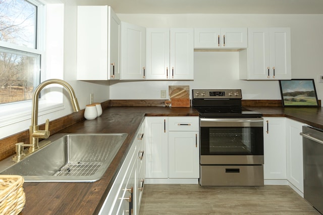 kitchen with appliances with stainless steel finishes, sink, wooden counters, white cabinets, and light hardwood / wood-style flooring