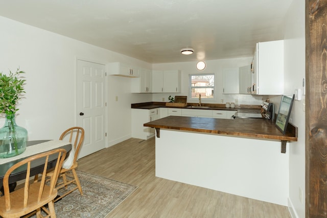 kitchen with sink, light hardwood / wood-style flooring, wooden counters, stove, and white cabinetry