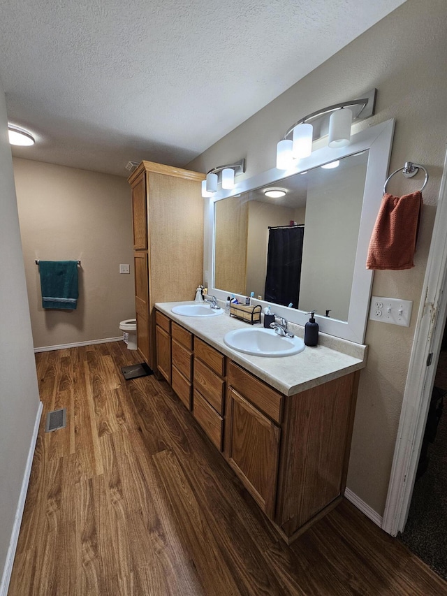 bathroom with wood-type flooring, vanity, a textured ceiling, and toilet