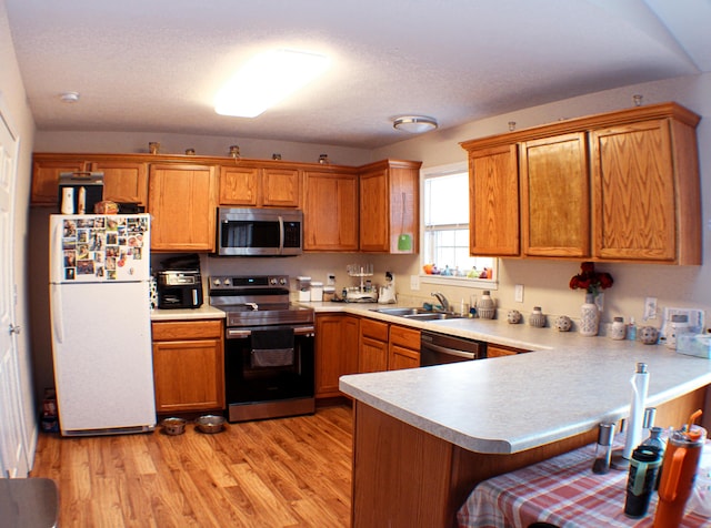 kitchen featuring appliances with stainless steel finishes, sink, light hardwood / wood-style flooring, and kitchen peninsula