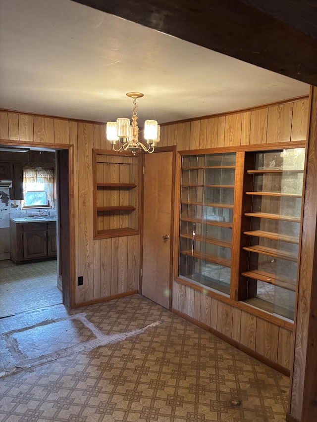 unfurnished dining area featuring a notable chandelier, wooden walls, and sink