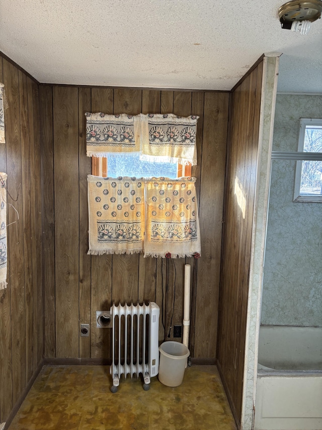 empty room with radiator heating unit, a textured ceiling, and wood walls