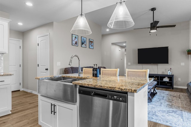 kitchen featuring sink, dishwasher, light stone counters, an island with sink, and white cabinets