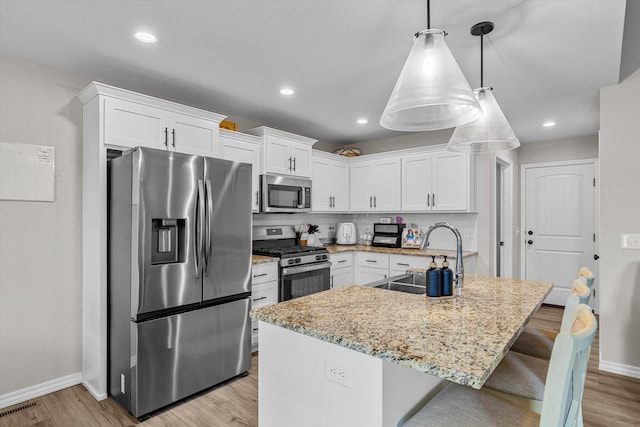 kitchen featuring sink, stainless steel appliances, white cabinets, decorative light fixtures, and light wood-type flooring