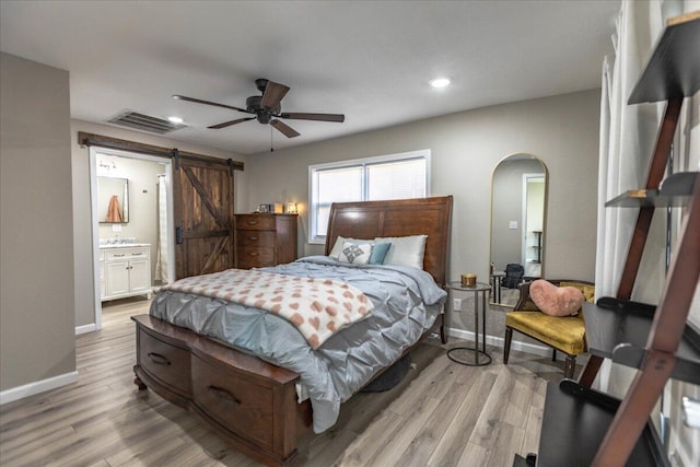 bedroom with a barn door, connected bathroom, ceiling fan, and light hardwood / wood-style flooring