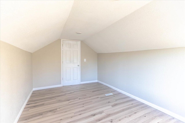 additional living space with lofted ceiling, light hardwood / wood-style floors, and a textured ceiling