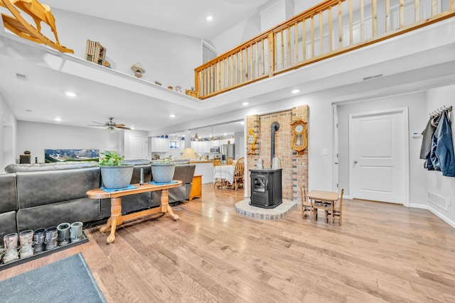 living room featuring a towering ceiling, a wood stove, ceiling fan, and light wood-type flooring