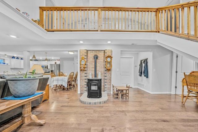 living room featuring light wood-type flooring, a high ceiling, and a wood stove