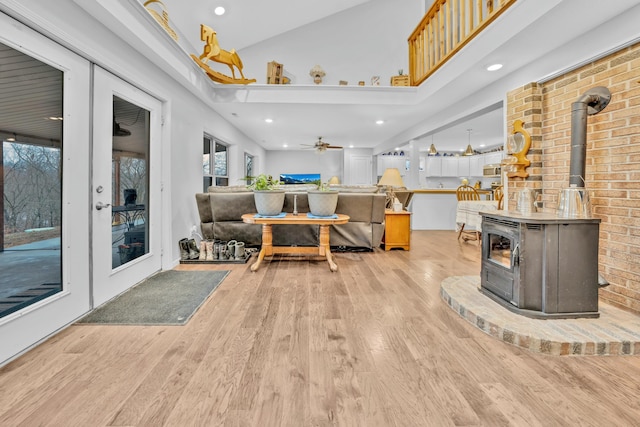 living room featuring ceiling fan, high vaulted ceiling, a wood stove, and light wood-type flooring