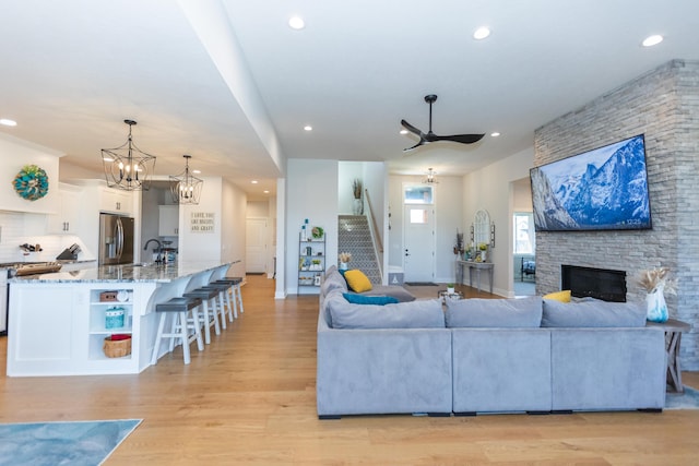 living room with ceiling fan with notable chandelier, a fireplace, sink, and light hardwood / wood-style flooring