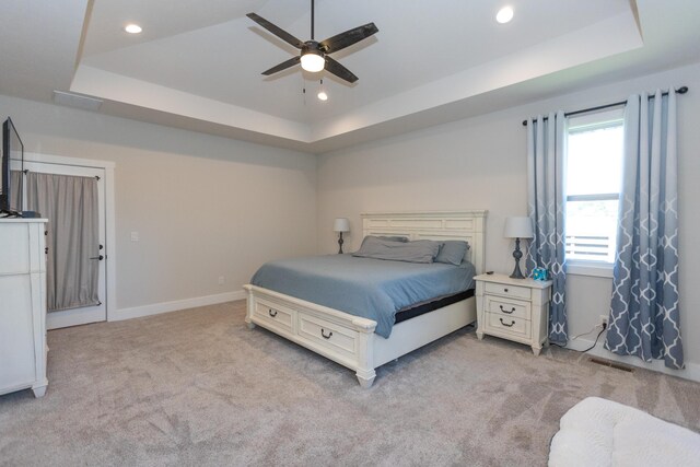 bedroom featuring a raised ceiling, light colored carpet, and ceiling fan