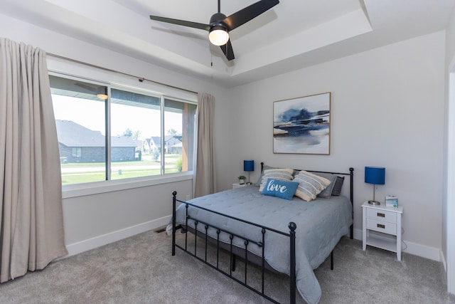 carpeted bedroom featuring a raised ceiling and ceiling fan