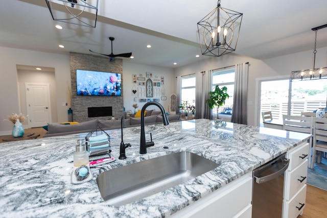 kitchen with pendant lighting, a fireplace, white cabinetry, sink, and light stone counters