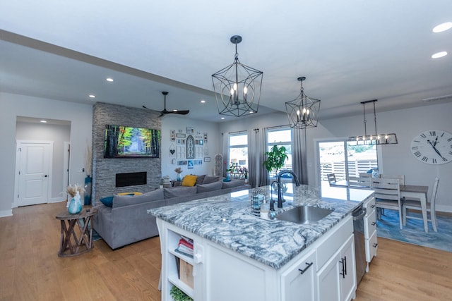 kitchen with sink, a kitchen island with sink, a stone fireplace, and white cabinets