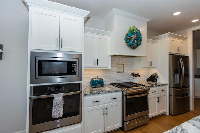 kitchen featuring light wood-type flooring, white cabinets, stainless steel appliances, light stone countertops, and backsplash