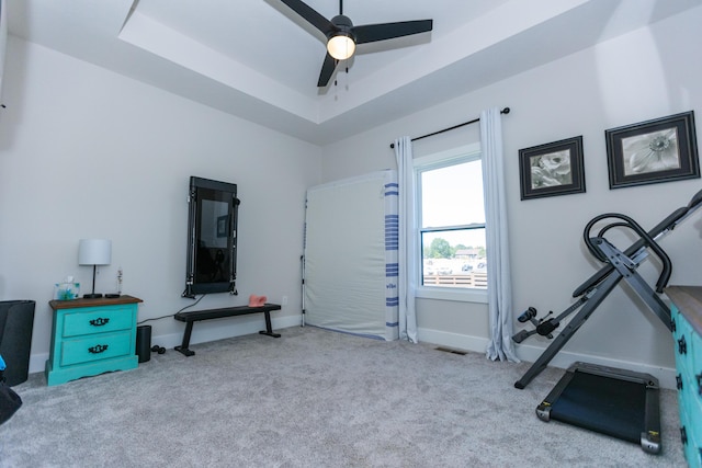 workout area with a raised ceiling, light carpet, and ceiling fan