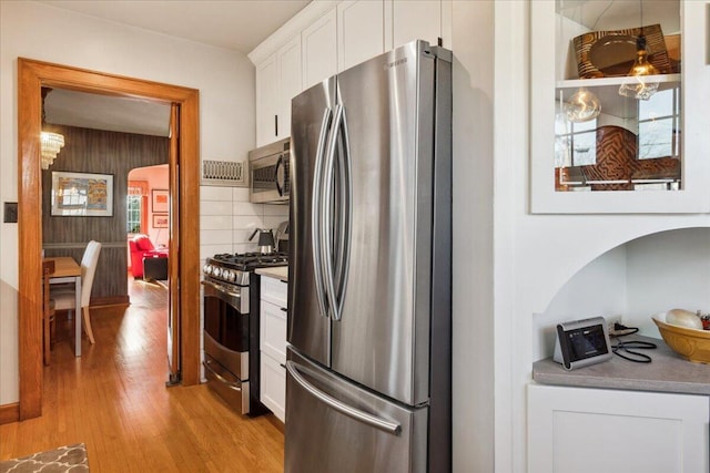 kitchen featuring backsplash, light hardwood / wood-style floors, white cabinets, and appliances with stainless steel finishes