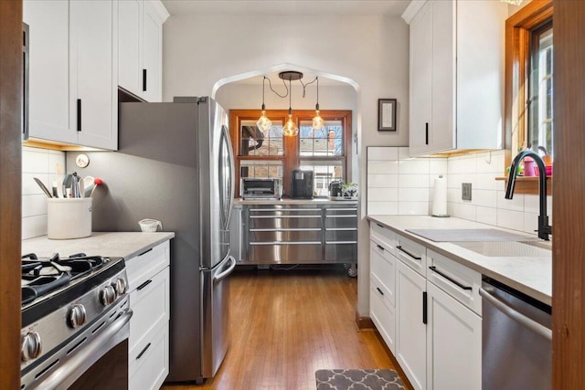 kitchen featuring pendant lighting, sink, appliances with stainless steel finishes, white cabinets, and light wood-type flooring