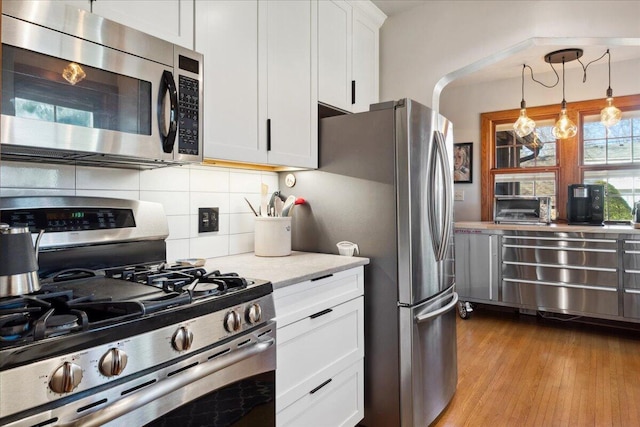 kitchen featuring tasteful backsplash, decorative light fixtures, light hardwood / wood-style flooring, appliances with stainless steel finishes, and white cabinets