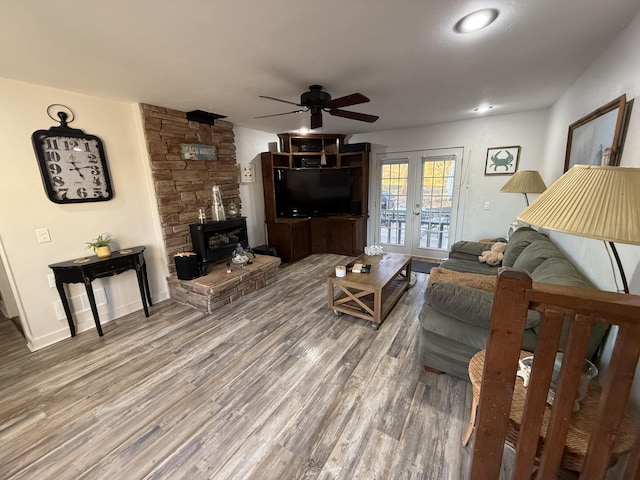 living room with wood-type flooring, a wood stove, ceiling fan, and french doors