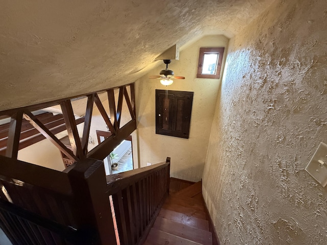 stairway featuring a textured ceiling, vaulted ceiling, and wood-type flooring