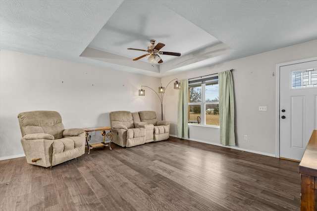 living room with a tray ceiling, wood-type flooring, a textured ceiling, and ceiling fan