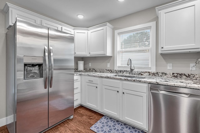 kitchen with sink, dark wood-type flooring, appliances with stainless steel finishes, white cabinetry, and light stone counters