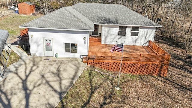 back of property with an outbuilding, a deck, a shingled roof, and a storage unit