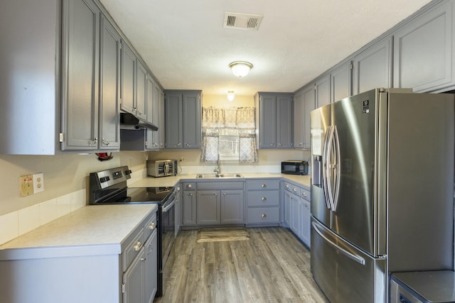 kitchen with visible vents, gray cabinetry, appliances with stainless steel finishes, a sink, and under cabinet range hood